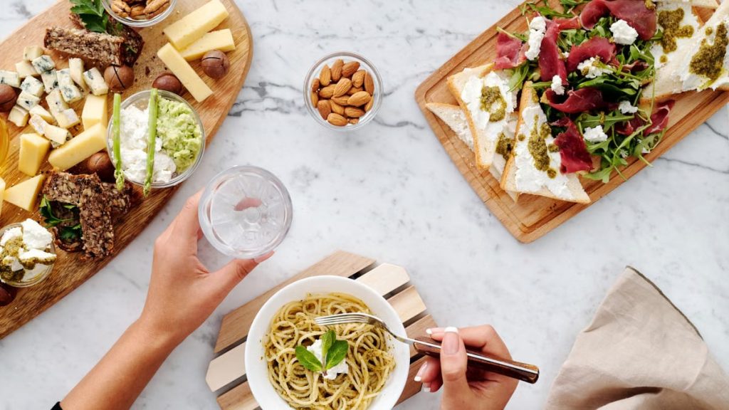 Delicious flat lay of gourmet cheese board, pasta, and appetizers on marble table.